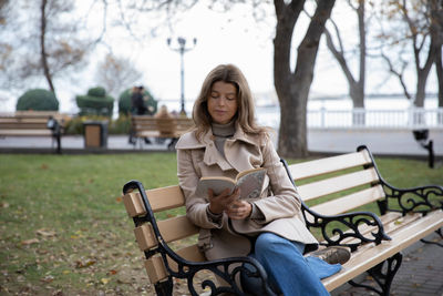 Portrait of young woman sitting on bench at park