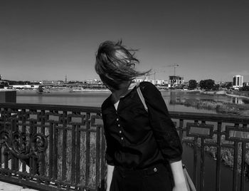 Woman with tousled hair in city against clear sky