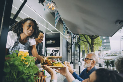 Smiling owners giving indian food to customers while standing in commercial land vehicle