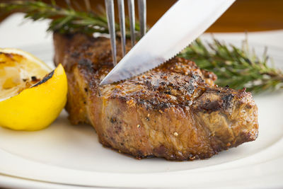 Close-up of knife and fork on grilled steak with rosemary herb and lemon in plate