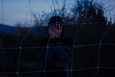 Man hiding face with hands seen through net during dusk