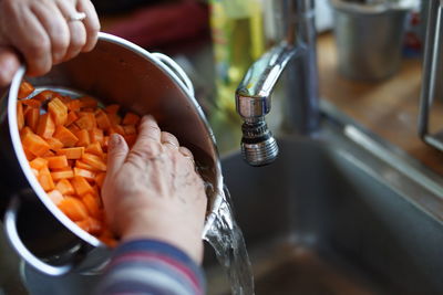 Cropped hands washing carrots in kitchen sink