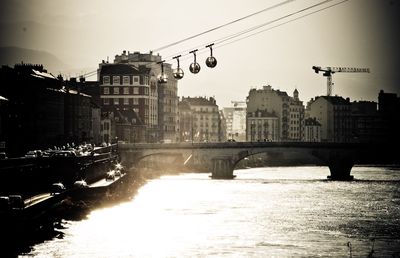 Bridge over river by buildings in city against sky