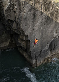 Male rock climber climbing up cliff above water