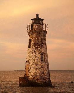 Old lighthouse in sea against sky during sunset