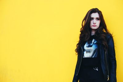 Portrait of young woman standing against yellow wall