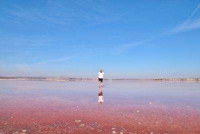 Rear view of man standing at beach against sky