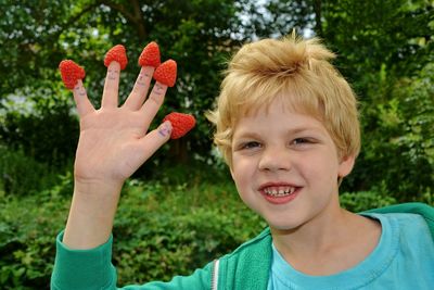 Portrait of boy with raspberries on fingers against trees