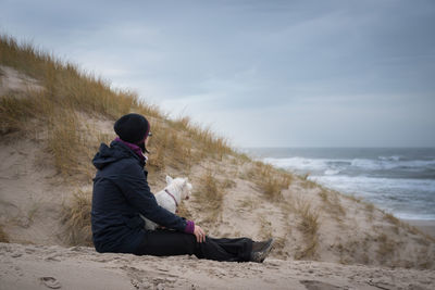 Rear view of man sitting on beach against sky