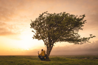 Rear view of woman sitting on field against sky during sunset