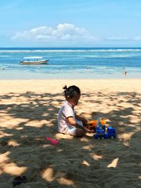 Boy sitting at beach against sky