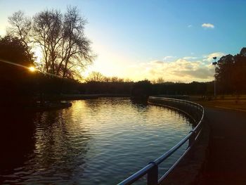 Swimming pool by trees against sky during sunset