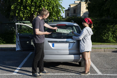 Man and woman putting learning plate on car