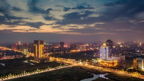 Illuminated city against cloudy sky at night