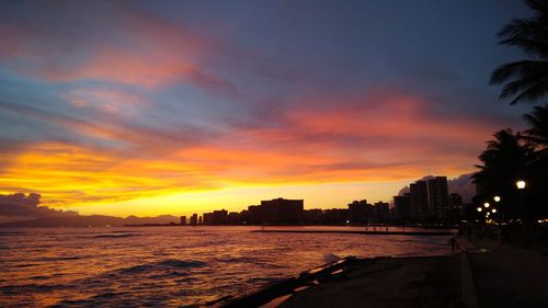 Silhouette buildings by sea against sky during sunset