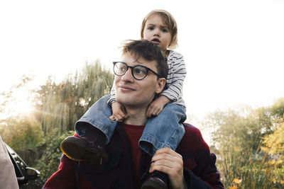 Smiling father wearing eyeglasses carrying daughter on shoulder