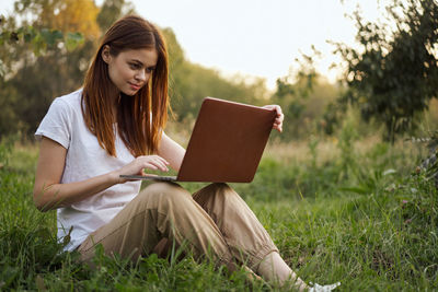 Woman using laptop while sitting on field