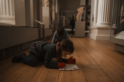 Rear view of girl sitting on floor at home
