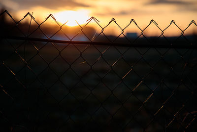 Close-up of chainlink fence against sky during sunset