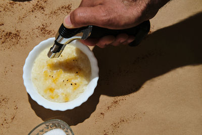 Hand with burner to burn the sugar on the rice pudding on a brown back