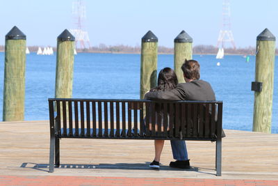 Rear view of people looking at pier on sea against clear sky