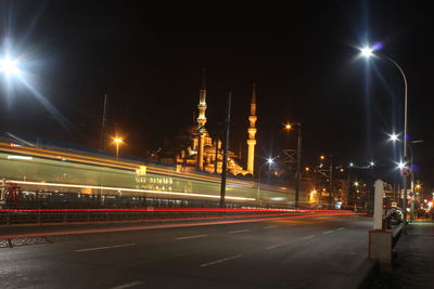 Light trails on road by mosque against clear sky at night