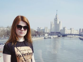 Portrait of young woman standing in city against sky