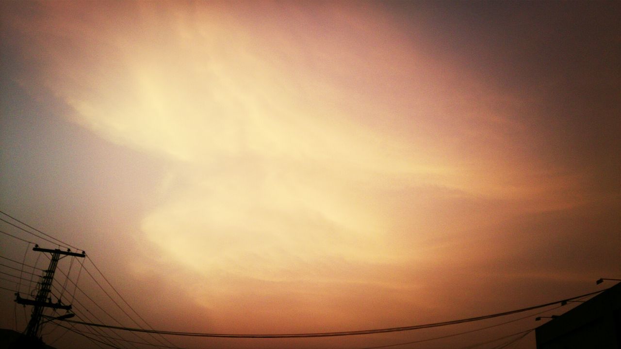 Low angle view of electricity pylon against orange sky