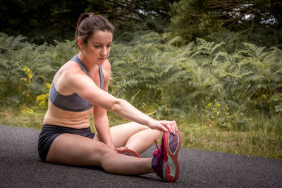 Full length of woman exercising while sitting on road