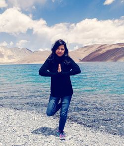 Portrait of young woman standing on lake shore against sky