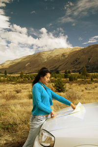 Woman looking at map on field against sky