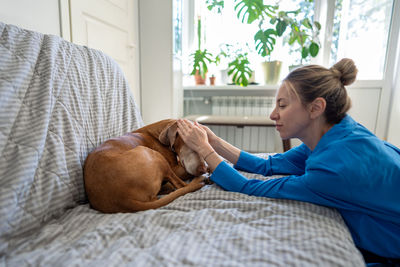 Side view of woman using mobile phone while lying on bed at home