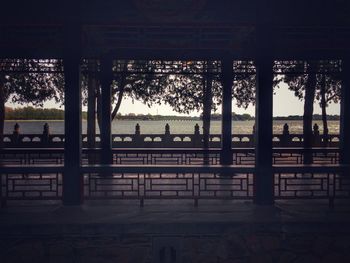 Silhouette people sitting on bench by river against trees