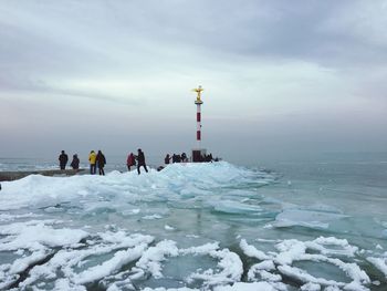 People by frozen sea against cloudy sky during winter