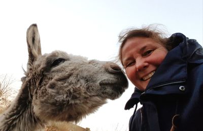 Portrait of smiling woman against clear sky with donkey