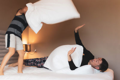 Playful boy and his father pillow fighting and having fun together at home.