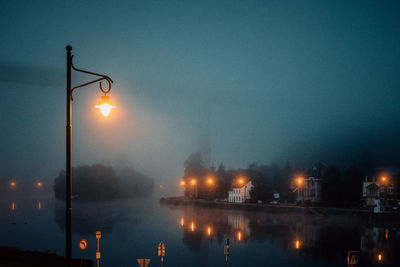 Illuminated street lights by river against sky at night