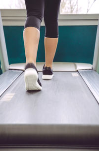 Low section of woman walking on treadmill in gym