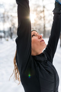 Woman with arms raised standing on snow covered land during winter