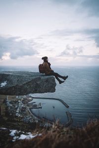 Woman sitting on cliff by sea against sky