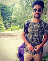 Portrait of young man wearing sunglasses standing against plants