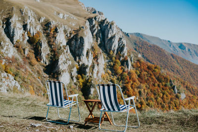 Chairs on rocks by road against sky