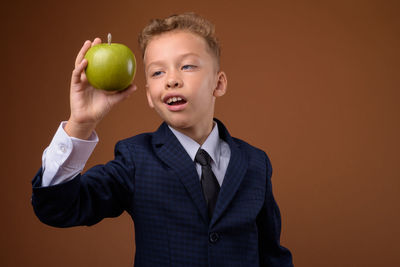 Full length of happy boy holding apple against orange background