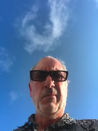 Low angle portrait of mature man wearing sunglasses against blue sky