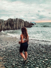 Rear view of woman standing on rock at beach against sky