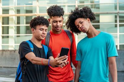 Young man holding smart phone while standing on laptop