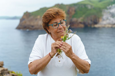 Senior woman smelling flowers against sea