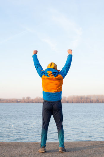 Rear view of man with arms raised standing by river