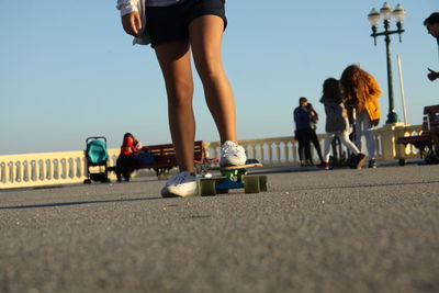 Low section of woman skateboarding on road against clear blue sky during sunset