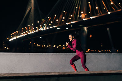 Full length of woman on illuminated bridge in city at night